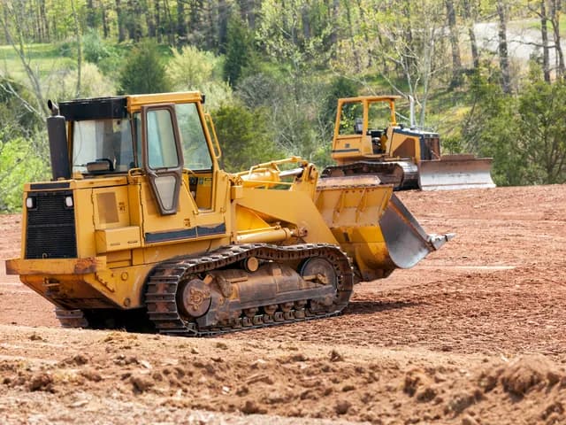 Tracked loader and dozer on exposed ground beside woodland, from Battlefield Landworks’ supplied photo collection